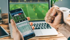 Sports Betting User Victorious Holding Mobile Infront of Laptop 